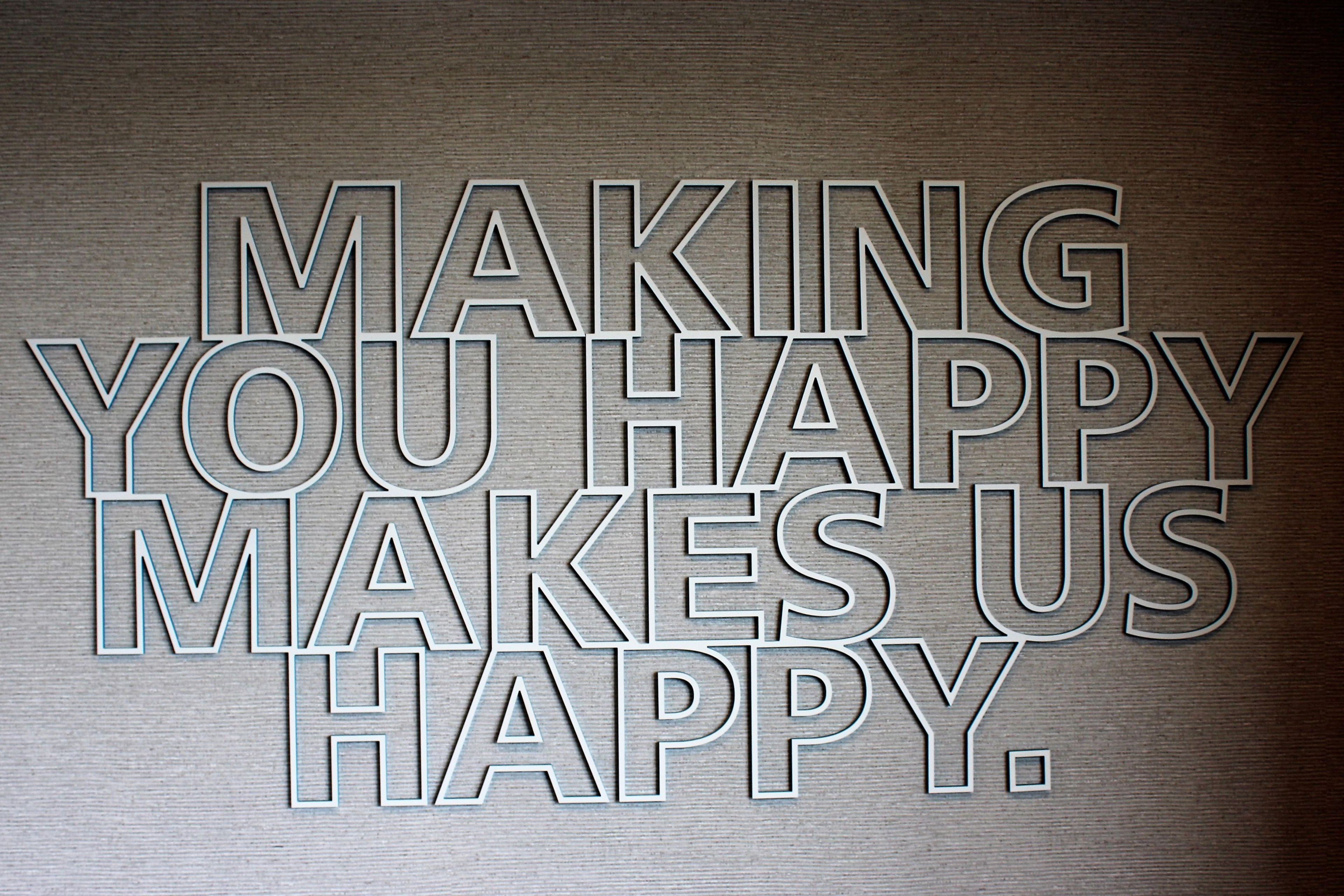 A metallic wall with embossed text that reads 'MAKING YOU HAPPY MAKES US HAPPY.'