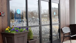 A building entrance with a glass door, a bench outside, and a planter with flowers. - Hampton Inn Lexington, NC (Lexington)