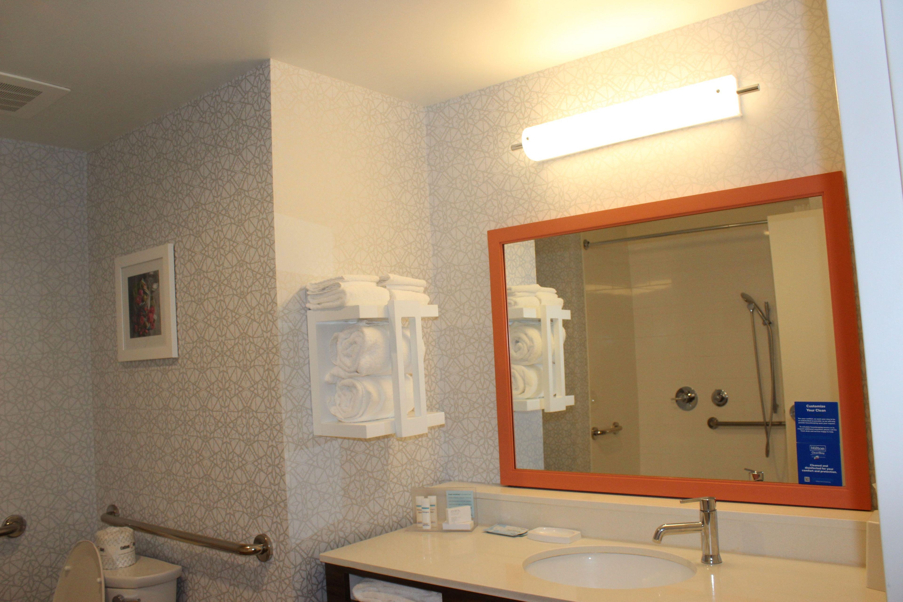 Une salle de bain d’hôtel avec un grand miroir, un lavabo et un porte-serviettes.