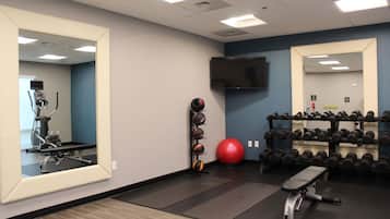 Une salle de sport équipée de matériel d’exercice, d’un miroir, d’un téléviseur et d’un porte-haltères fixé au mur.