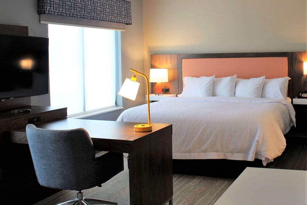 A hotel room with a bed, a desk, a chair, a TV, and a window.