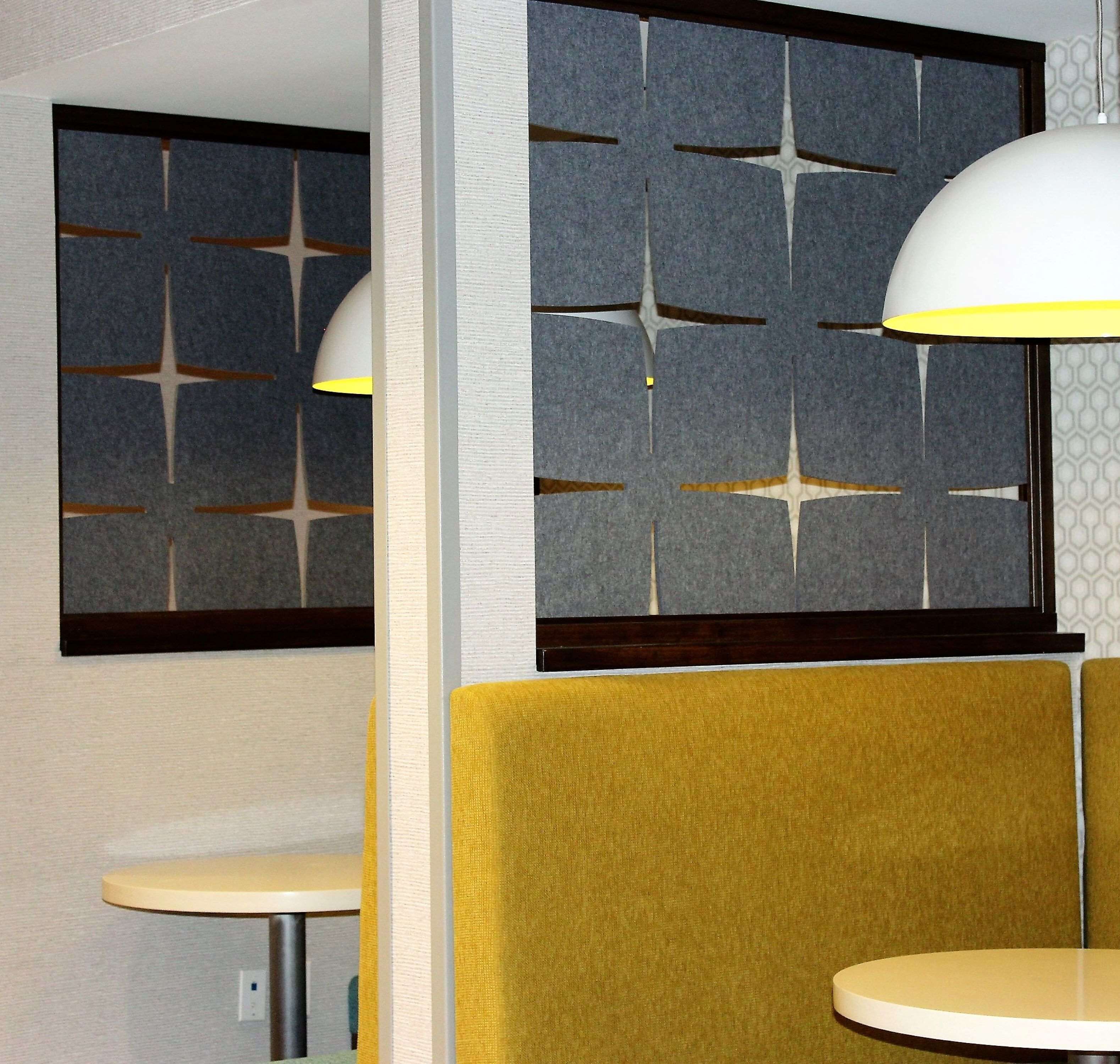 A modern interior with a round table and a yellow booth, a wall-mounted light fixture, and a geometric patterned wall.