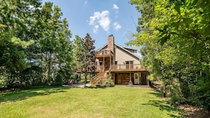 A two-story house with a wooden deck and a stone chimney, surrounded by lush greenery. - River Front House on Black River in Georgetown SC (Georgetown)