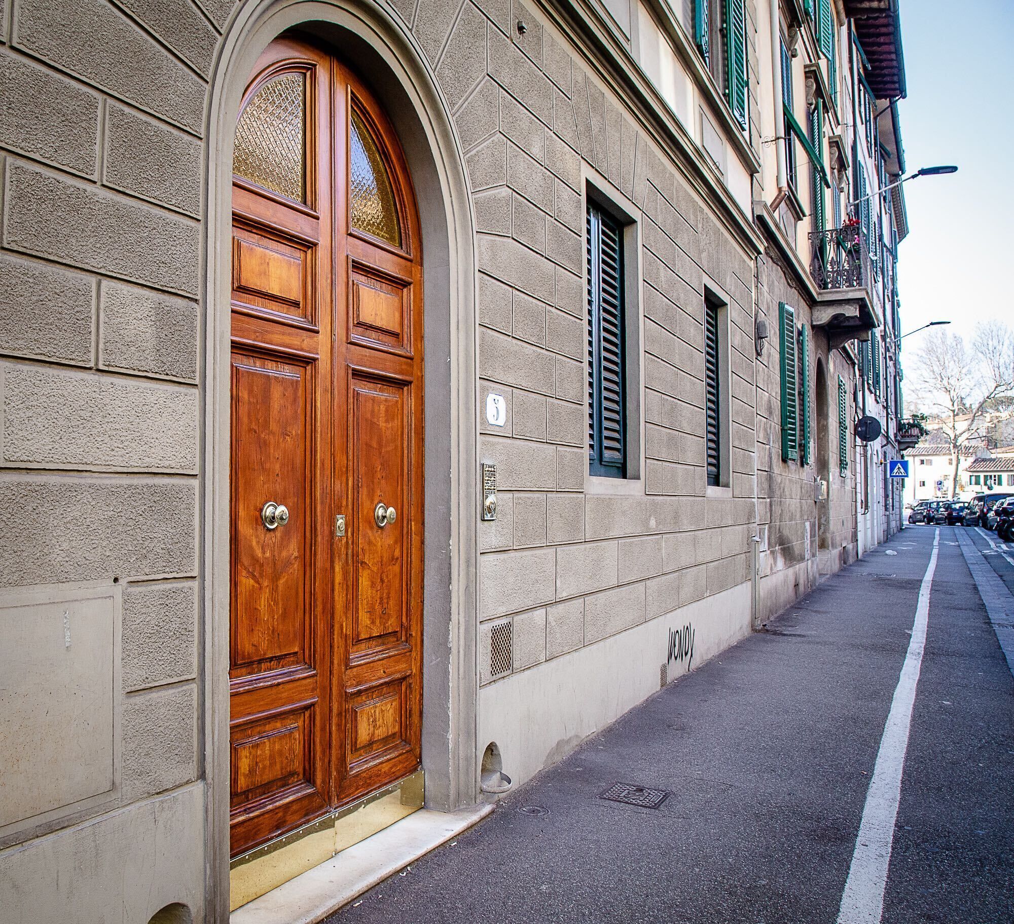 A building with a large wooden double door, a stone facade, and a narrow sidewalk.