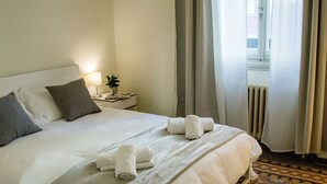 Ein ordentlich bezogenes Bett mit Handtüchern, ein Nachttisch mit Lampe und ein gestreifter Boden.