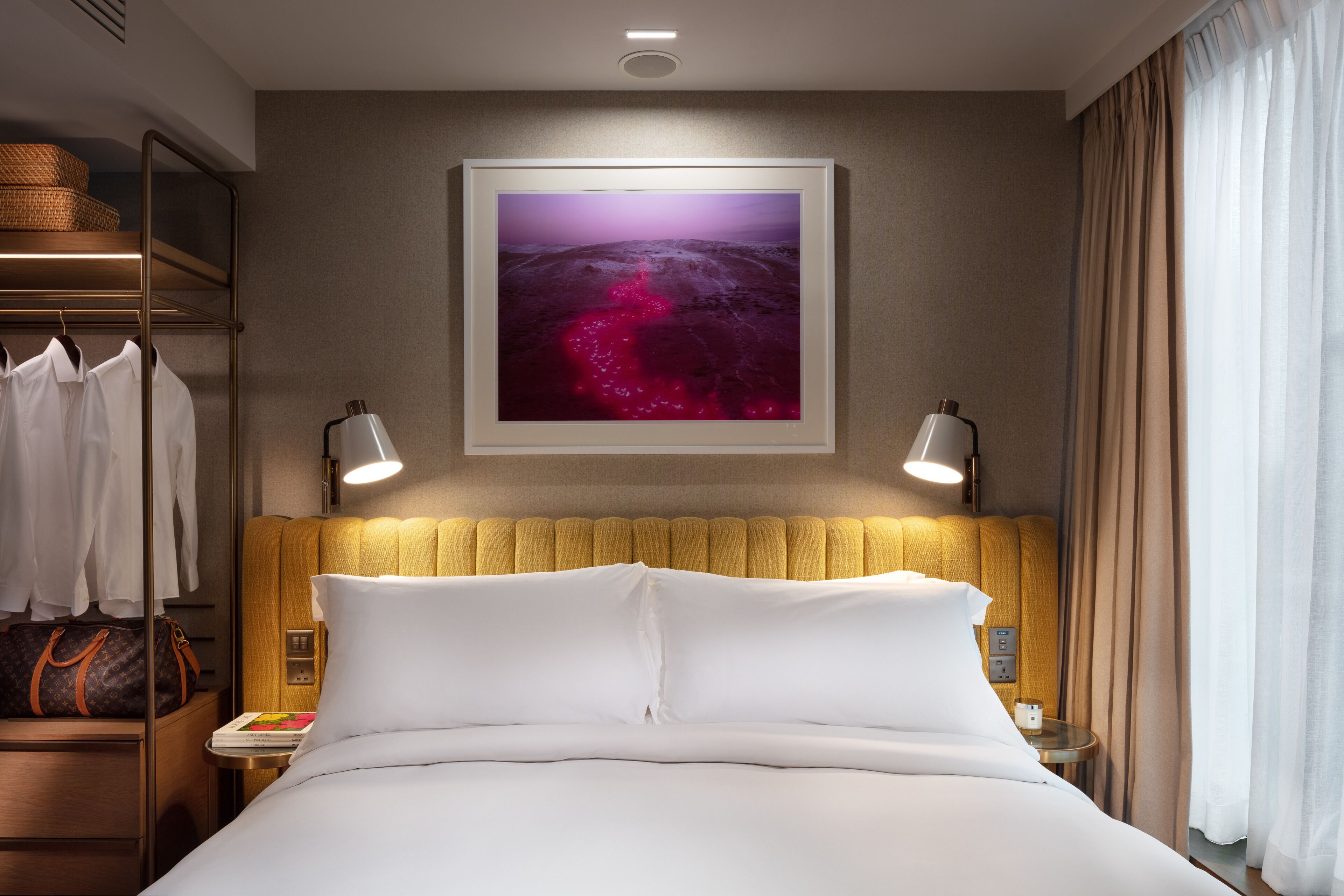 A hotel room with a bed, a headboard, a wall-mounted TV, a nightstand, a lamp, and a window with curtains.
