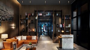 A modern lobby with a leather sofa, marble coffee table, and bookshelves filled with books and decorative items. - The Hari Hong Kong (Hong Kong)
