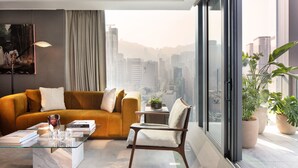 A modern living room with a glass coffee table, a sofa, a chair, and a large window offering a city view. - The Hari Hong Kong (Hong Kong)