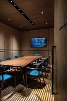Un salón de conferencias con una larga mesa de madera, sillas azules, iluminación empotrada en el techo y un cuadro abstracto grande en la pared, además de una alfombra estampada.