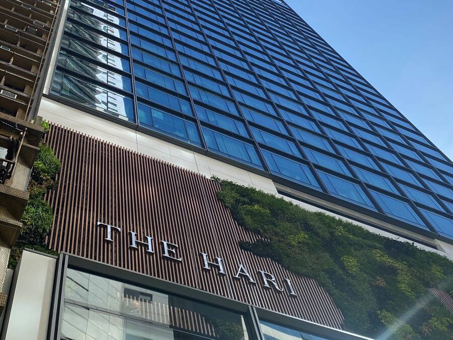 A modern building with a reflective glass facade and a sign reading "THE HARI".