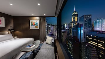 A hotel room with a bed, a small table, and a view of a cityscape at night.