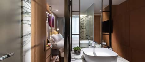A modern bathroom with a marble sink, wooden paneling, a large mirror, and a view into the bedroom.