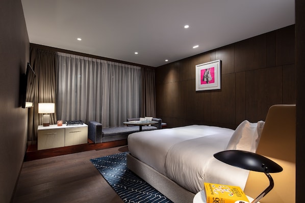 Una habitación de hotel moderna con una cama grande, un escritorio, una silla, un televisor y una ventana con cortinas.