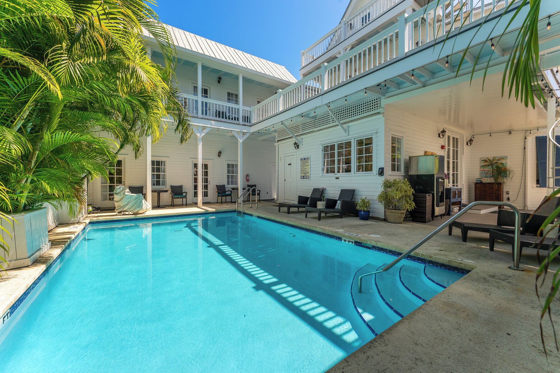 A pool area with a clear blue pool, lounge chairs, and a covered seating area with a view of the building.