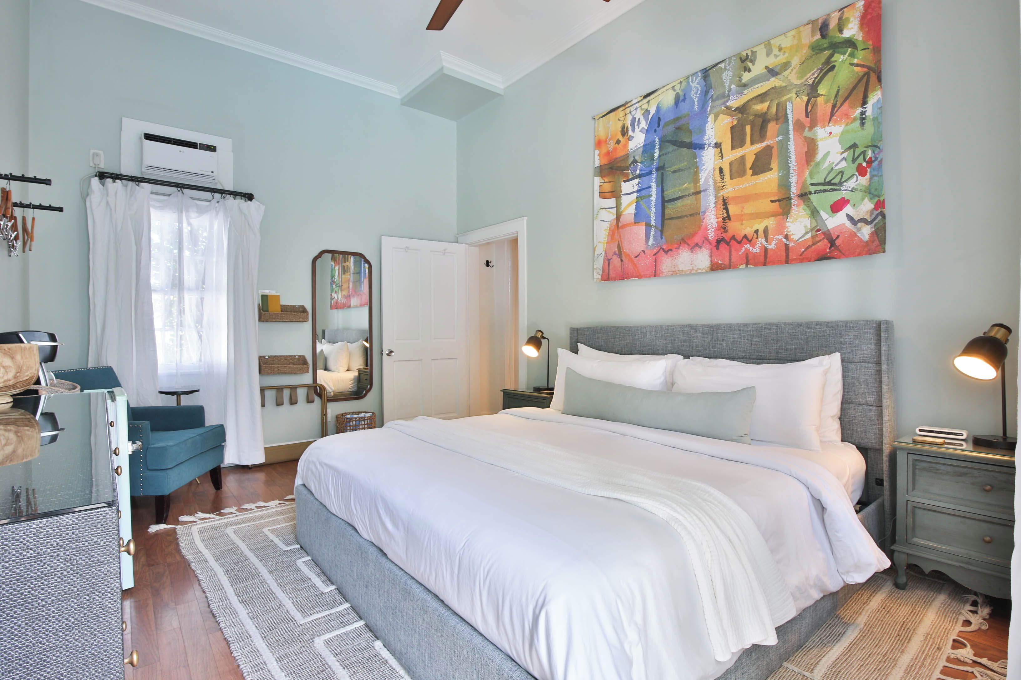 A bedroom with a large bed, bedside lamps, a dresser, a mirror, and a painting on the wall.