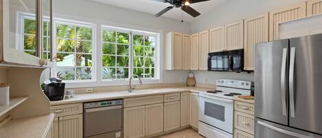 A modern kitchen with white cabinets, stainless steel appliances, a dishwasher, an oven, and a ceiling fan.