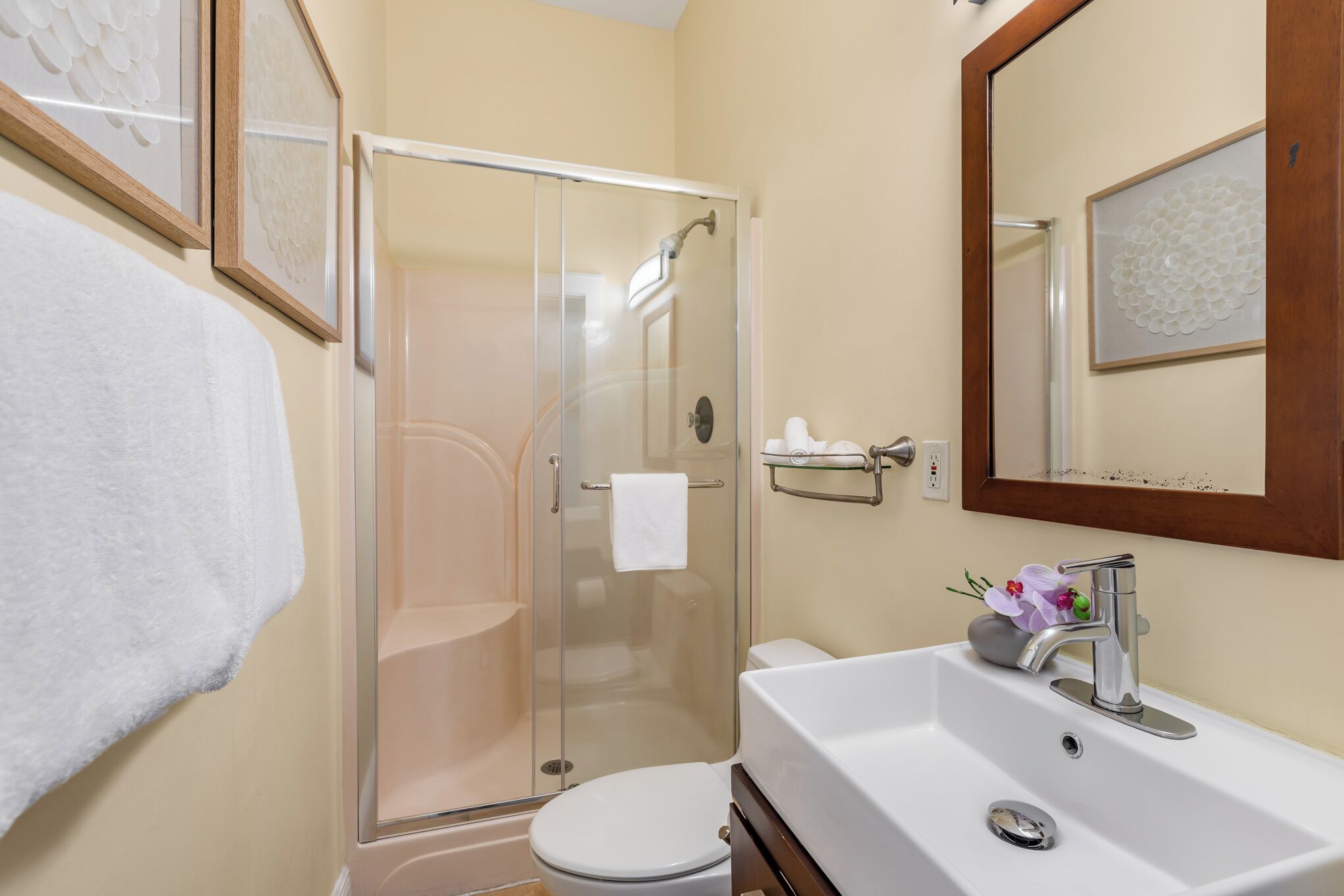 A bathroom with a glass-enclosed shower, a white toilet, and a sink with a mirror above it.