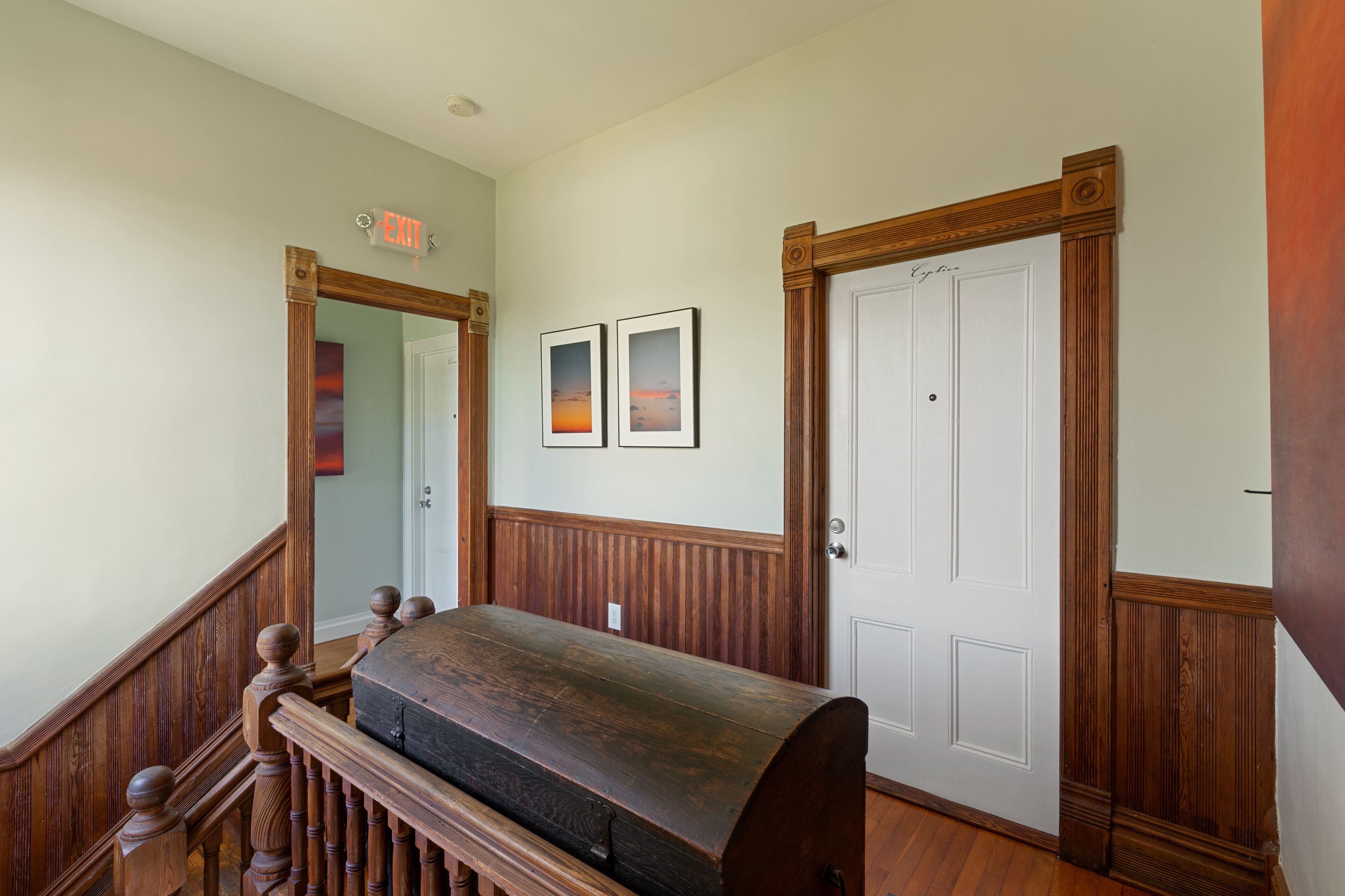 A hallway with a wooden bench, two framed pictures on the wall, and a white door with a wooden frame.