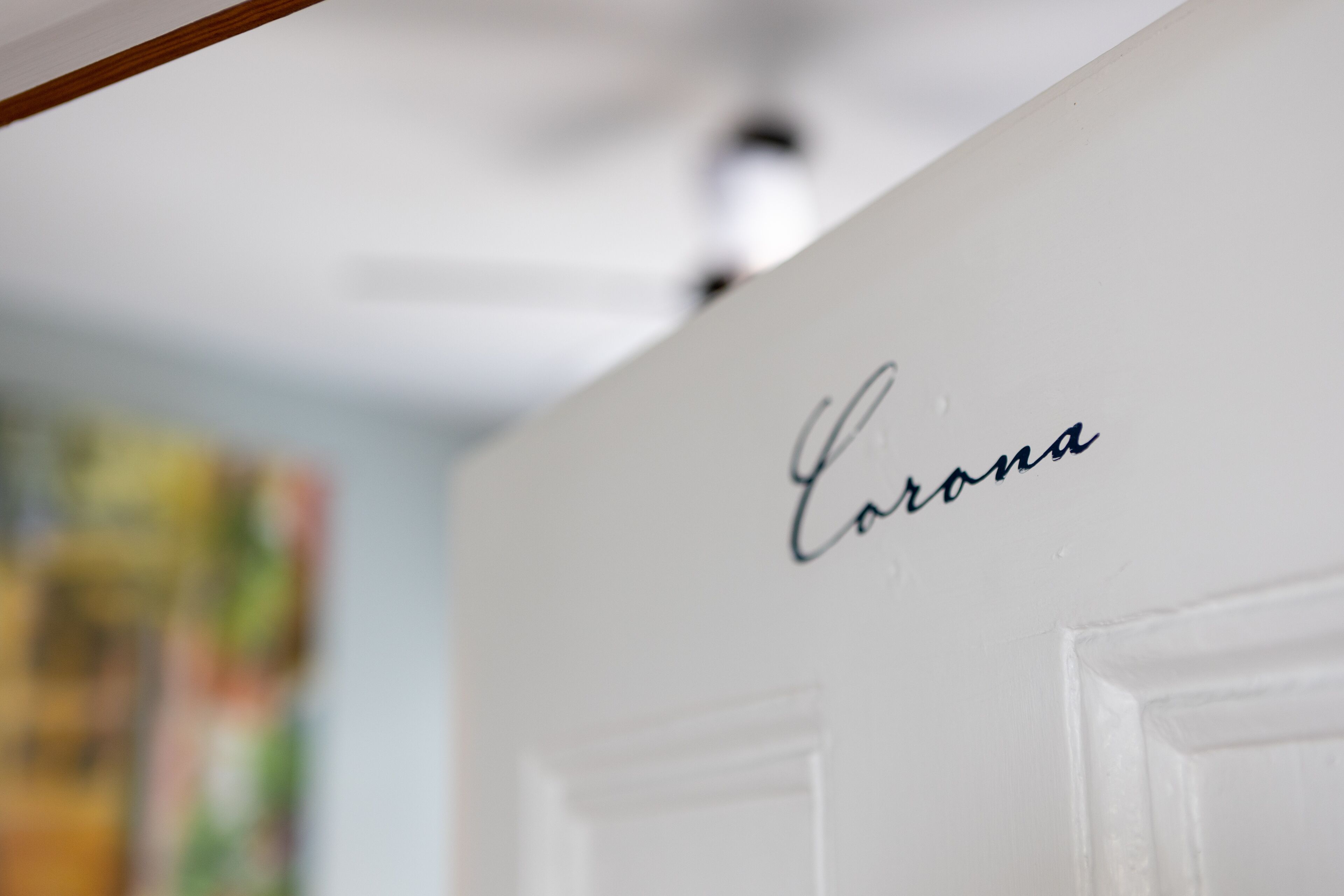 A white wall with the word "Corona" written in cursive.