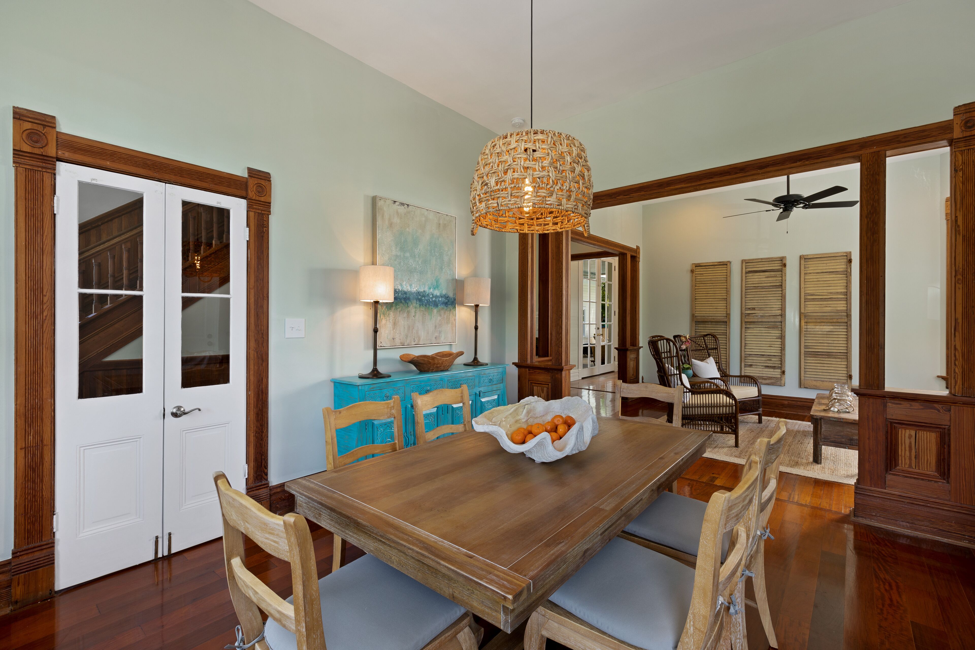A dining area with a wooden table and chairs, a hanging light fixture, and a staircase in the background.