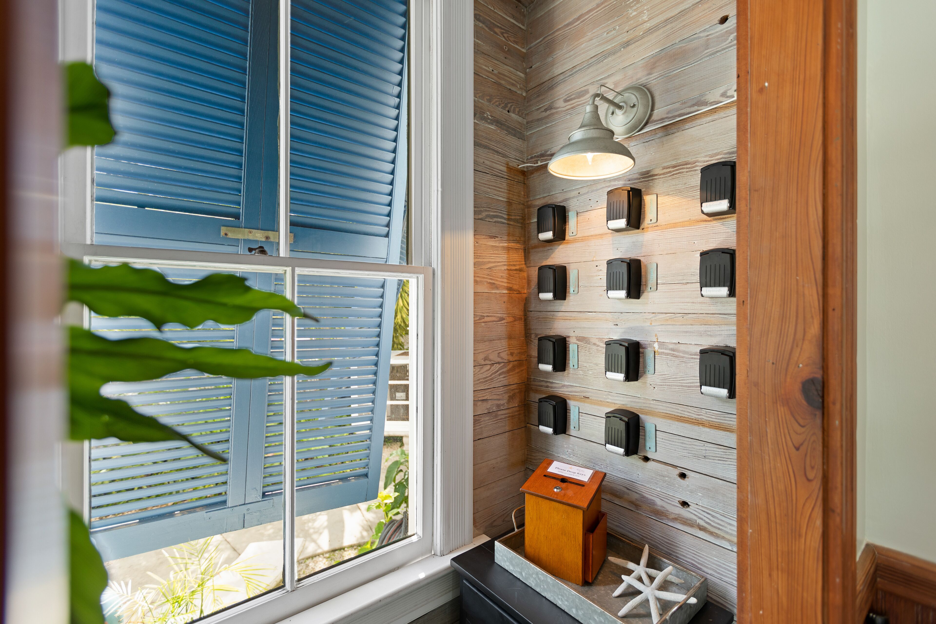 A room with a wooden wall, a window with blue shutters, and a wall-mounted light fixture.