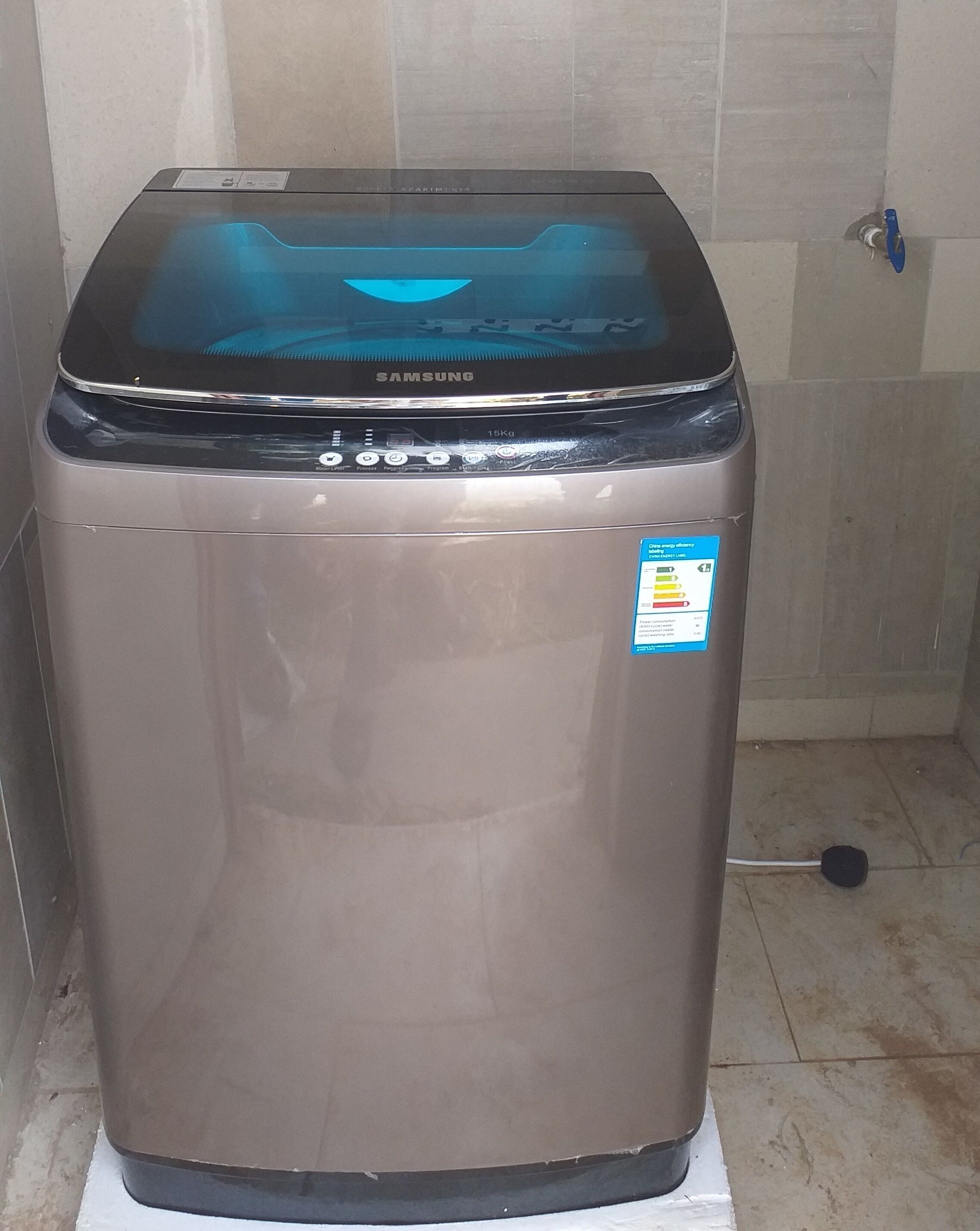 A Samsung refrigerator in a kitchen with tiled walls and a blue door handle.
