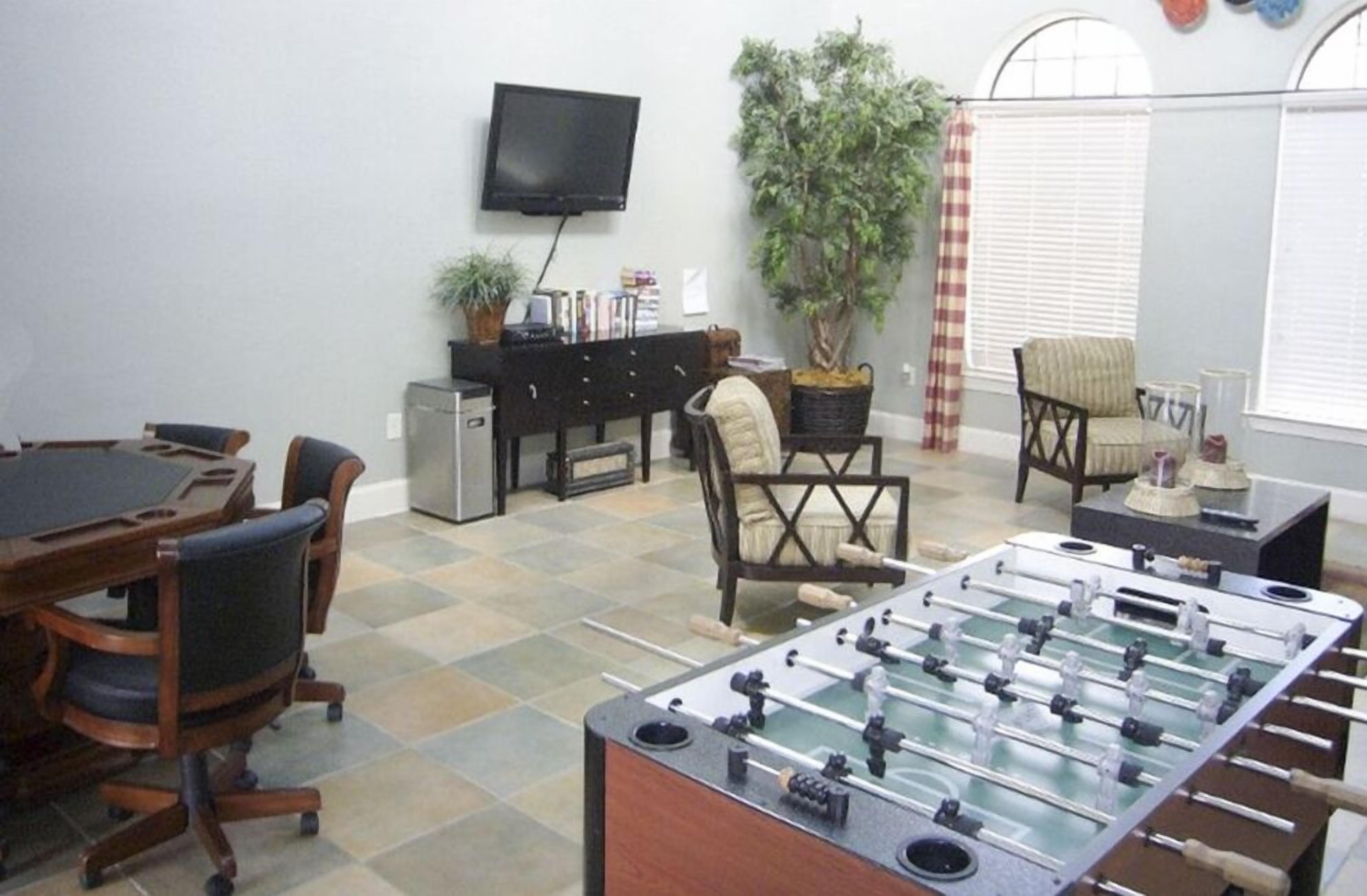 A room with a foosball table, a television, a desk with a computer, and a large plant.