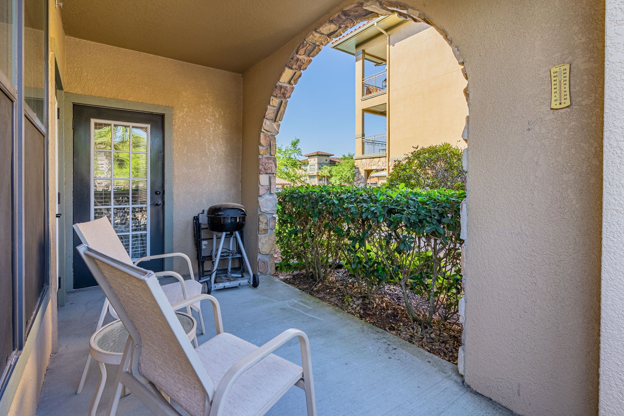 A covered patio with two white chairs, a grill, and a stone archway.