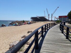 A wooden boardwalk leading to a beach with a lifeguard tower and a beach bar.