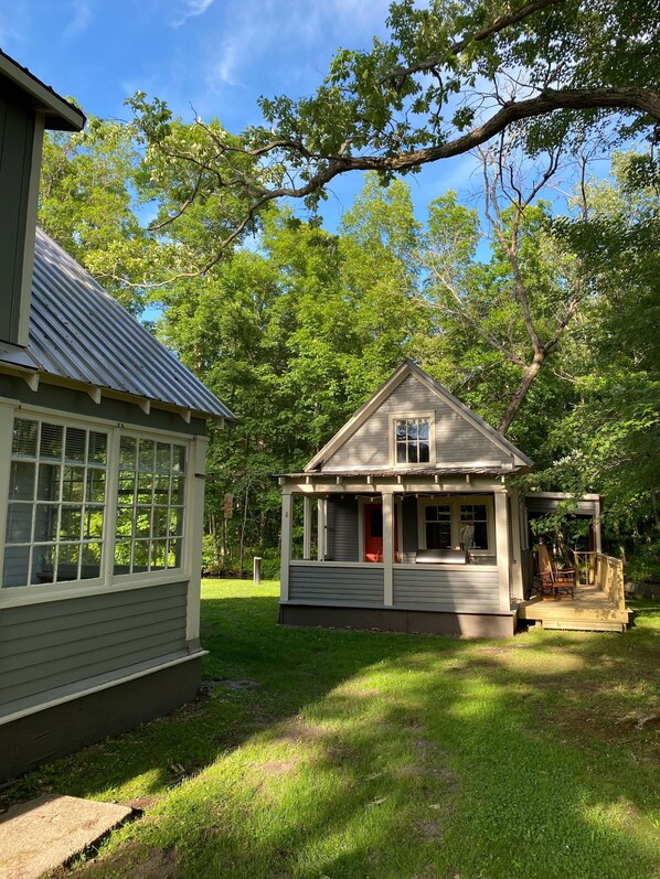 A small wooden cabin with a porch and a covered outdoor seating area, surrounded by lush greenery. - Creek Side Cottage with Lake Views, Lake Access, Dock and Secluded Yard (Jamestown)