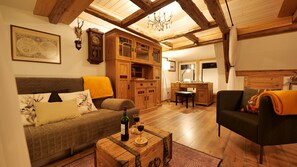 A cozy living room with a sofa, a coffee table with a bottle and glass, a wooden cabinet, and a desk with a chair.
