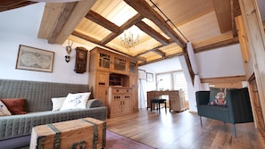 A spacious loft with exposed wooden beams, a large wooden cabinet, a grey sofa, and a green armchair.