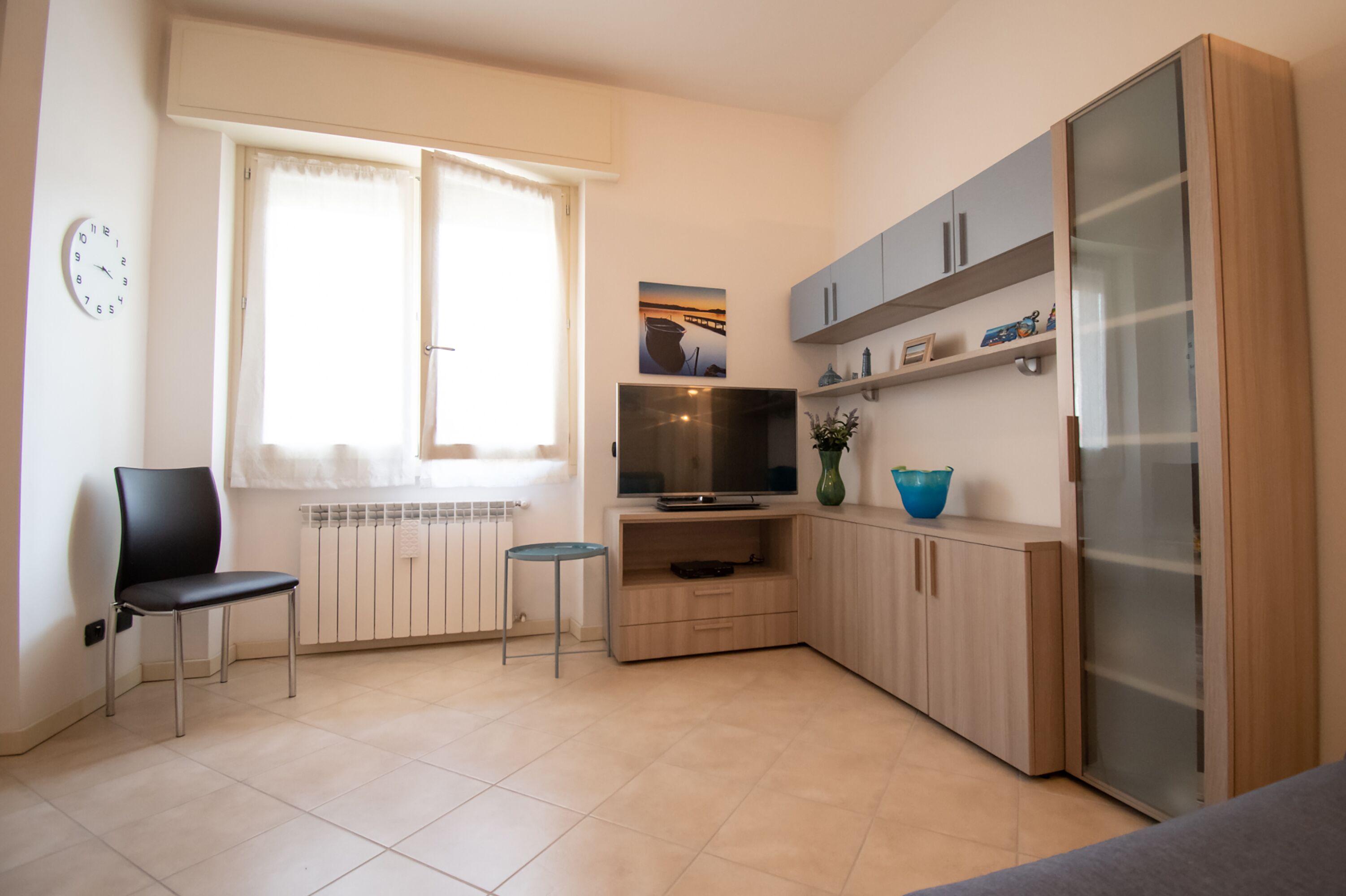 Un espacio habitable pequeño con un televisor, una silla, un radiador y un armario con estantes.