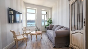 Una sala de estar con un sofá, dos sillones, una mesita, un televisor montado en la pared y vistas al exterior a través de amplios ventanales.