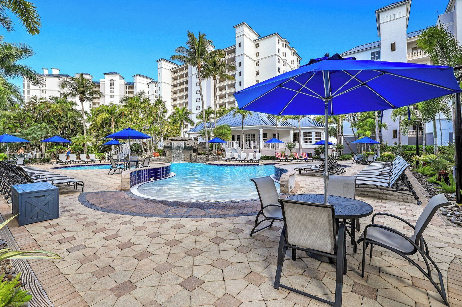 A pool area with lounge chairs, umbrellas, and a stone-tiled patio.