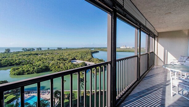 A balcony with a view of a river and greenery, a pool, and a white chair. - Surf Colony - Vanderbilt Beach - Bayside (Naples)