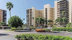 A multi-story hotel with a modern architectural design, featuring balconies on each floor and a parking area with cars and palm trees. - Surf Colony - Vanderbilt Beach - Bayside (Naples)