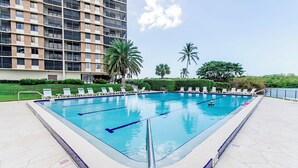 A rectangular swimming pool with lane dividers, surrounded by lounge chairs and palm trees, with a high-rise building in the background. - Surf Colony - Vanderbilt Beach - Bayside (Naples)
