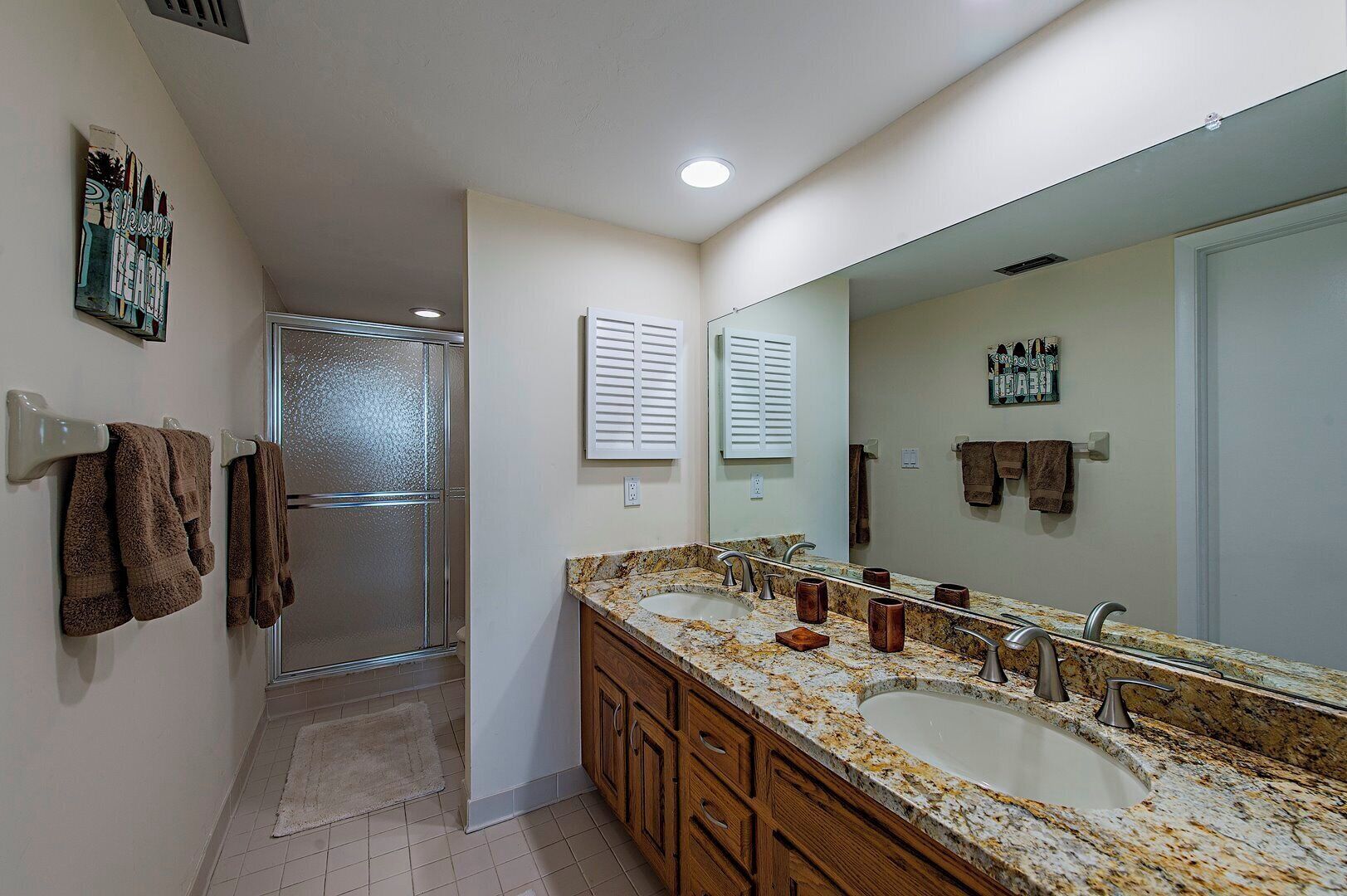 A bathroom with a large mirror, two sinks, and a shower.