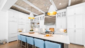 A modern kitchen with white cabinets, a large island with bar stools, pendant lighting, and a wooden ceiling. - Spacious Porch with Pool and Firepit (Panama City Beach)