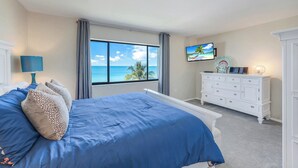 A bedroom with a large bed, a TV, a dresser, and a window with a view of the ocean.