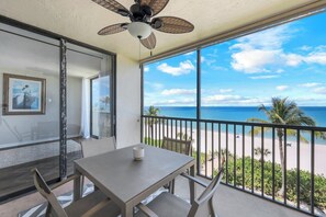 Uma varanda com mesa, cadeiras, ventoinha no teto e vista para a praia.