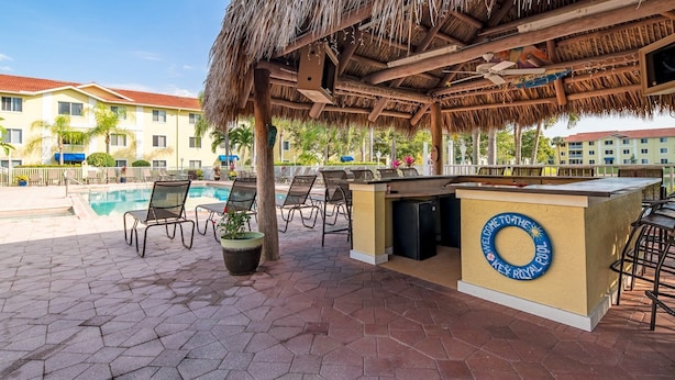 A poolside area with lounge chairs, a bar, and a thatched roof structure. - Key Royal - William Raveis Rentals (Naples)