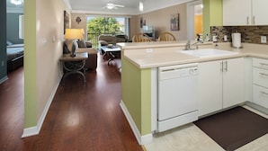 A modern kitchen with a dishwasher, white cabinets, and a dining area with a table and chairs. - Key Royal - William Raveis Rentals (Naples)