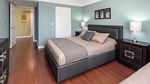 A bedroom with a bed, nightstands, a dresser, and a door leading to another room. - Key Royal - William Raveis Rentals (Naples)