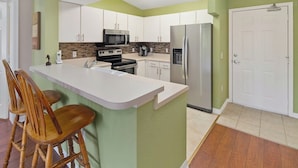 A modern kitchen with a central island, white cabinets, a stainless steel refrigerator, and a microwave. - Key Royal - William Raveis Rentals (Naples)