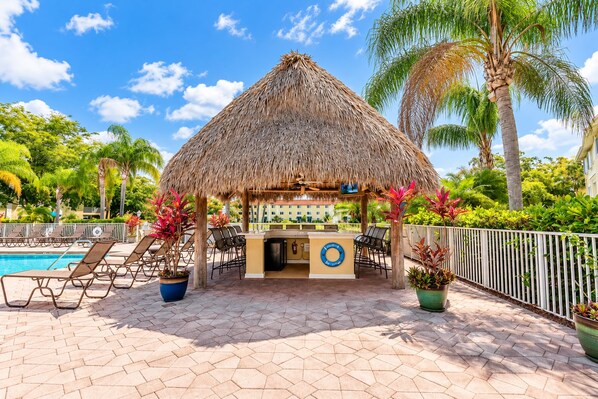A thatched-roof bar area with lounge chairs and a poolside setting.
