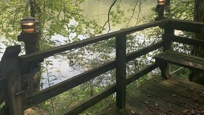 A wooden deck with railings overlooking a body of water, surrounded by trees. - Enjoy the River Breeze (Tompkinsville)