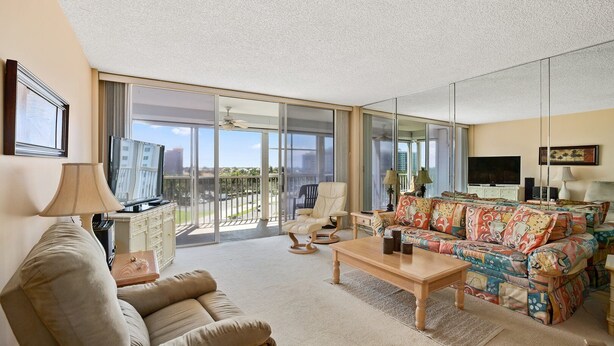 A spacious living room with a sofa, armchair, and coffee table, large sliding glass doors leading to a balcony, and a television. - Vanderbilt Towers - Walk to the Beach! (Naples)