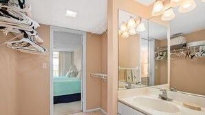 A hotel room with a bathroom, a bed with a blue bedspread, a large mirror, and a towel rack. - Vanderbilt Towers - Walk to the Beach! (Naples)